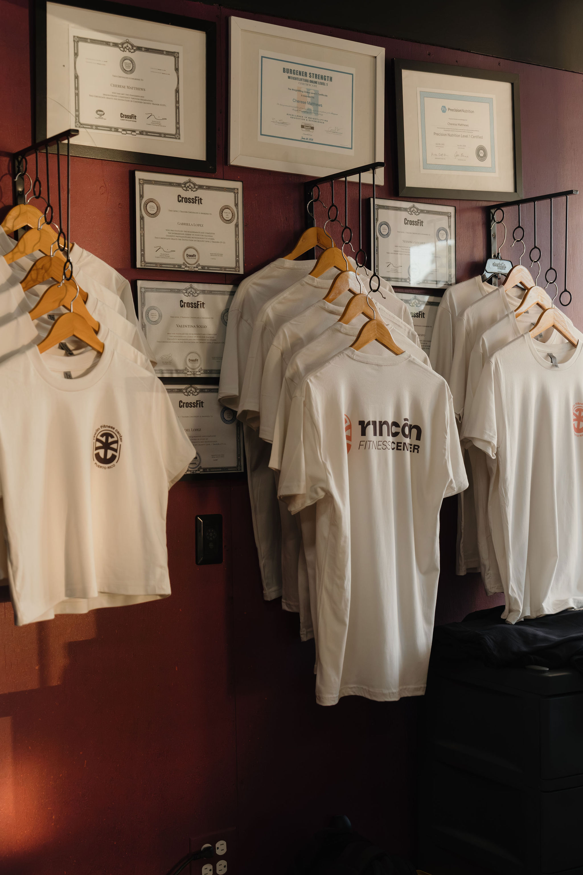Wall of CrossFit, Burgener Strength, and Precision Nutrition certifications next to RFC merch